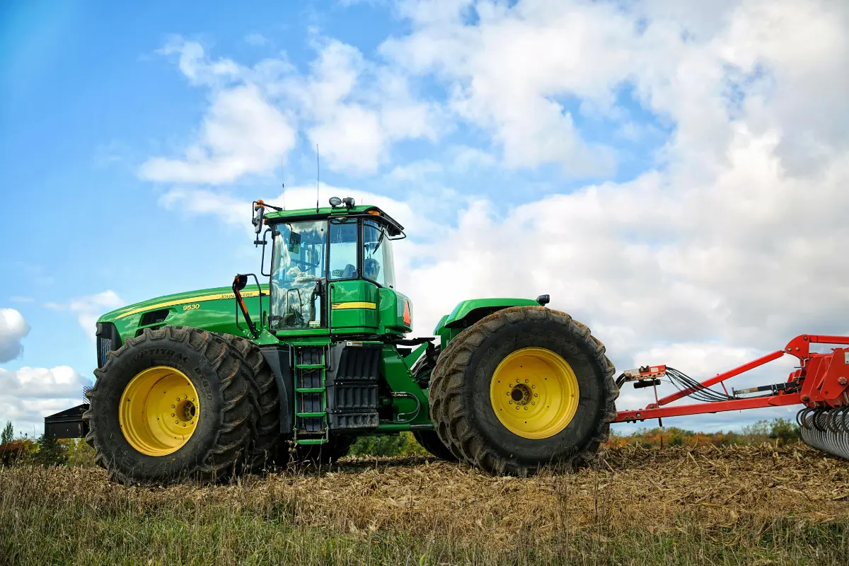 Green tractor pulling a red plow in a field – agricultural equipment repair in Sedalia, MO.