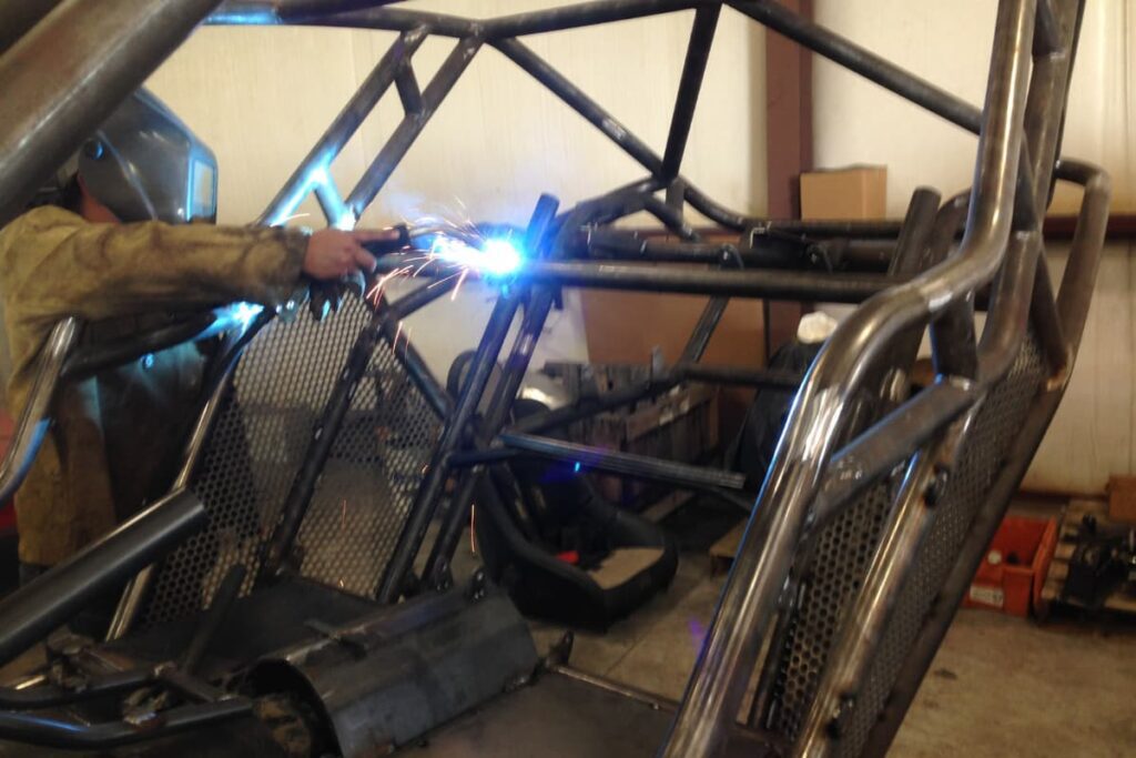Welder fabricating a custom roll cage for an off-road vehicle inside a metalworking shop.