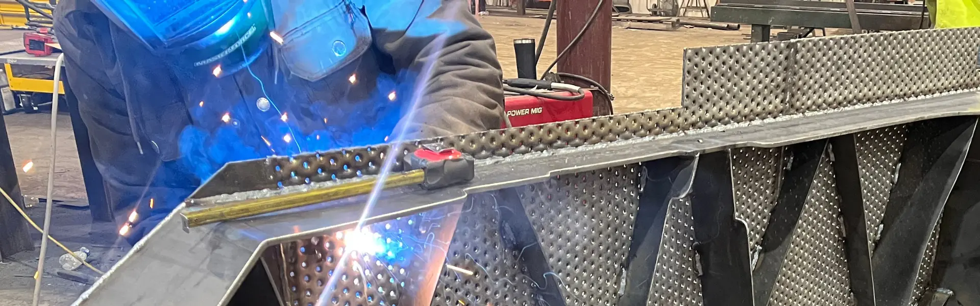 Welder working on diamond plate with sparks and blue welding arc.